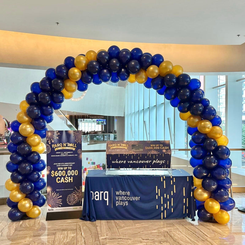 A spiral balloon arch with blue and gold balloons, set up over a table with promotional materials.1
