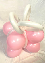 Load image into Gallery viewer, A festive balloon creation shaped like a gift box with pink balloons forming the base and white twisted balloons creating a ribbon bow on top