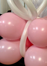 Load image into Gallery viewer, A festive balloon creation shaped like a gift box with pink balloons forming the base and white twisted balloons creating a ribbon bow on top