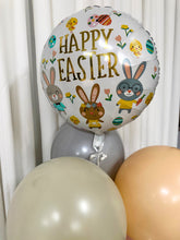 Load image into Gallery viewer, A festive Easter balloon bouquet featuring a large foil balloon with &#39;Happy Easter&#39; written in gold lettering, surrounded by illustrations of bunnies, eggs, and flowers. The foil balloon is complemented by pastel latex balloons in shades of cream, peach, sage green, and blush pink, tied together with ribbons against a white curtain backdrop.
