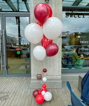 Load image into Gallery viewer, A bouquet of helium balloons in red, white, and maroon colors displayed in front of a store&#39;s entrance.
