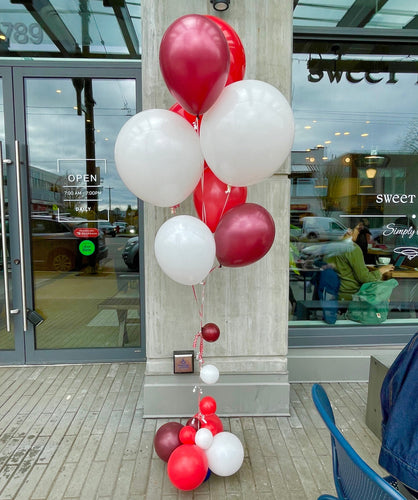 A bouquet of helium balloons in red, white, and maroon colors displayed in front of a store's entrance.