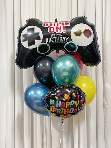 A bouquet of birthday balloons including a game controller supershape, chrome blue, green, red, yellow, black, and a 'Happy Birthday' gaming themed mylar balloon.