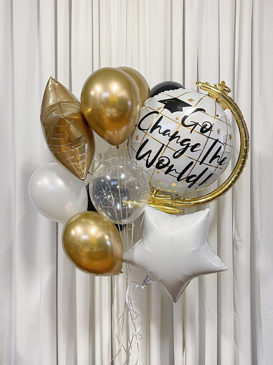 A bouquet of graduation balloons including a 'Go Change the World' globe balloon, a white star, a chrome gold star, and a variety of other balloons in chrome gold, pearl white, and clear with congratulation prints.