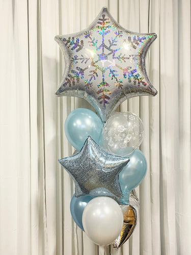 A bouquet of balloons featuring a large snowflake-shaped balloon, with smaller round balloons in blue and white shades, and decorative star-shaped balloons in silver and blue.